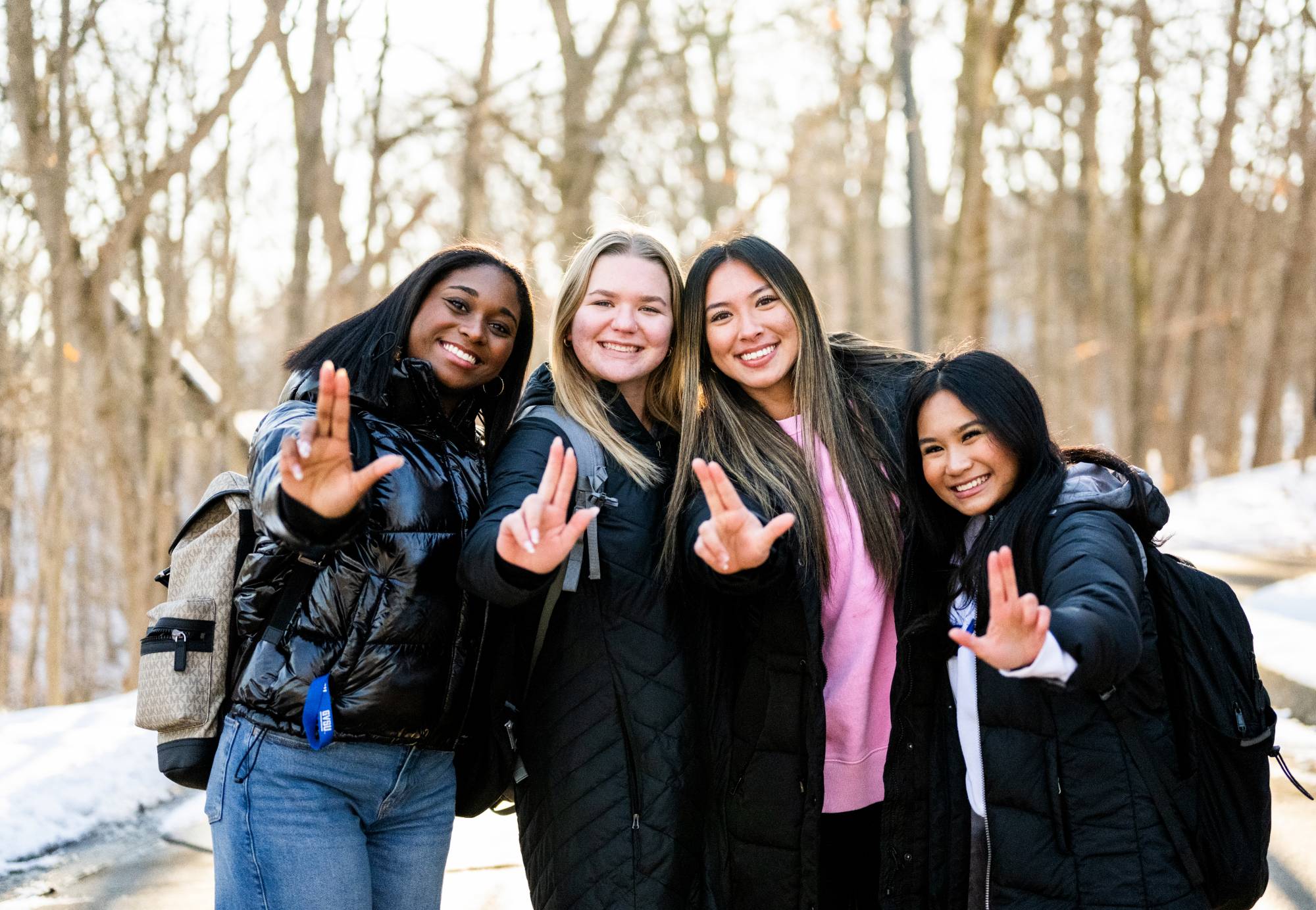 Four GVSU Students making the Laker sign with their hands on a sunny winter day.